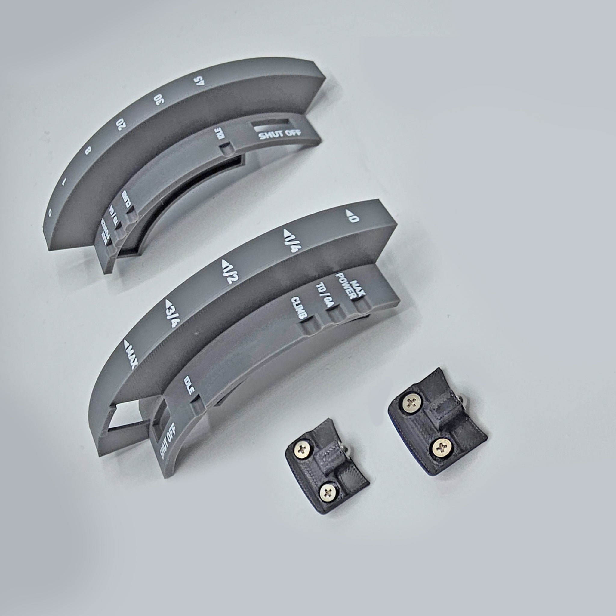 Gray plastic curved components with engraved text, similar to the levers from the Prodesksim "Add CRJ To Your Challenger Package," and two small rectangular pieces with screws are set on a light gray surface. The text includes words like "WASH," "RINSE," and "SHIFT." The layout is neatly organized, providing plenty of negative space.