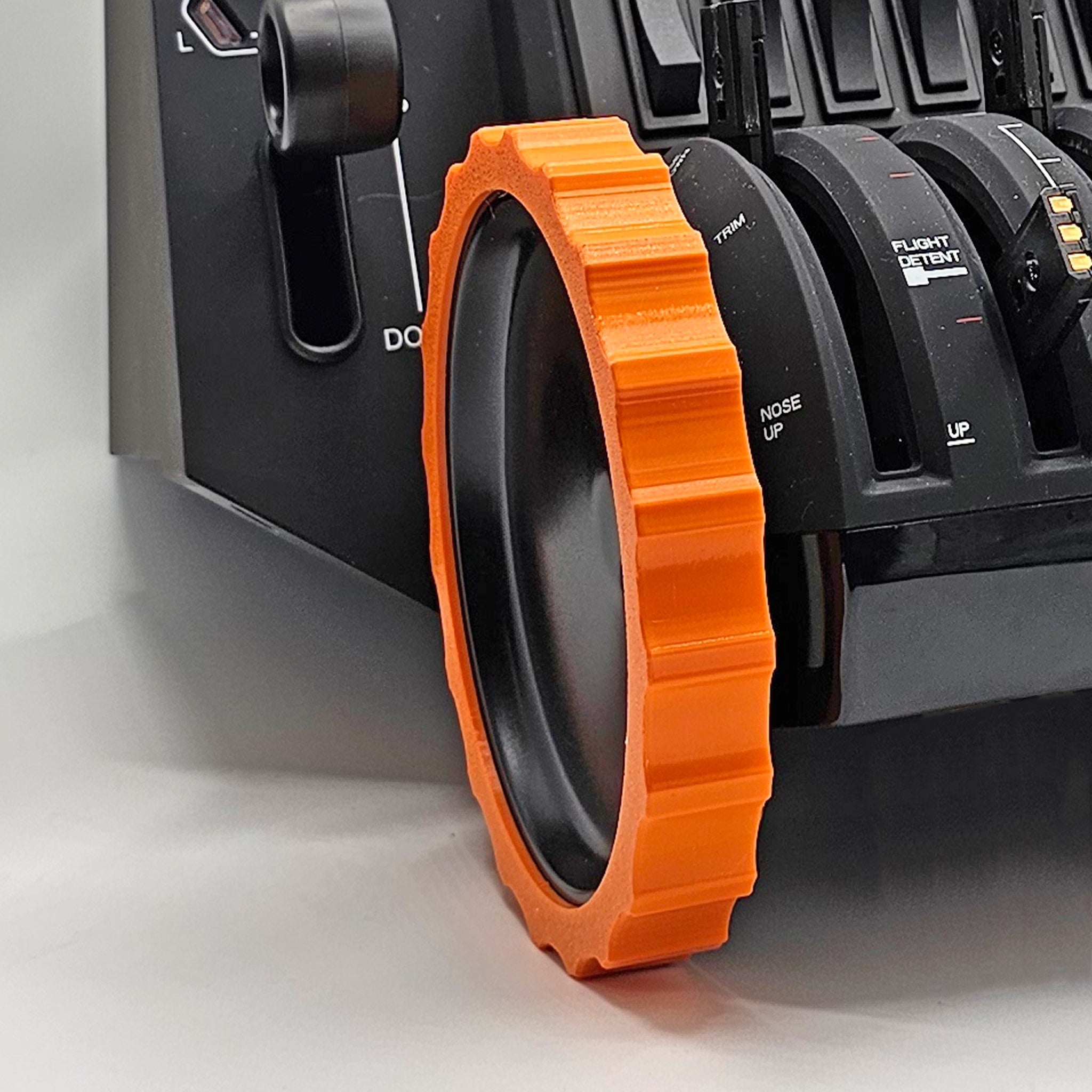 A close-up of the Prodesksim 1 Color Vibrant and Flexible Trim Wheel Cover for the Honeycomb Bravo Throttle Quadrant shows an orange, gear-like trim around the throttle lever. Perfect for flight simulation, this black device features various switches and labels visible in the background.