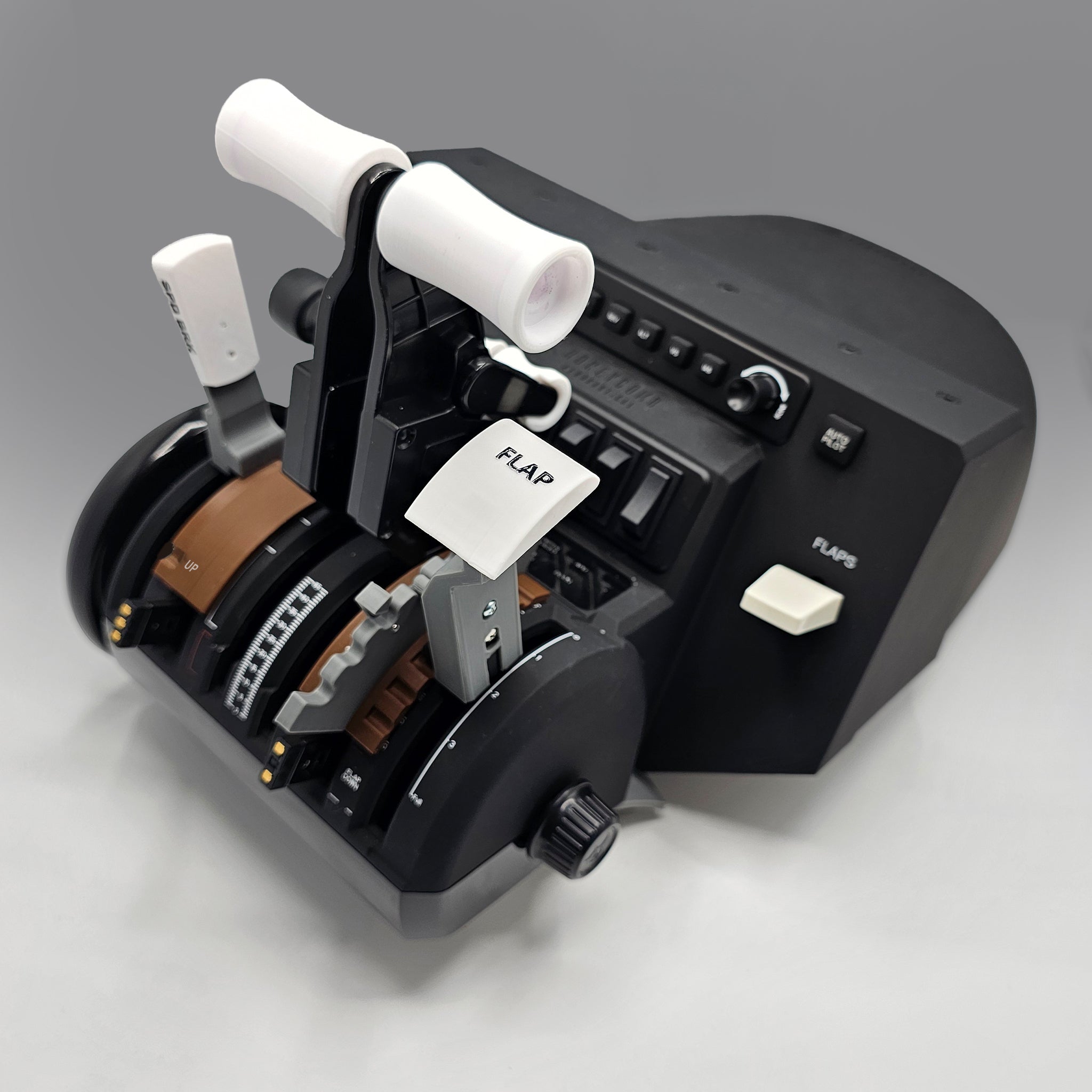 Close-up of a Boeing 777 Dual Action Detent/Spring mechanism throttle quadrant in black, designed by Prodesksim, featuring white levers and buttons. One lever is marked with a paper labeled "FLAP." The professional addon device for the HoneyComb Bravo throttle/VR rests on a light gray surface, showcasing its precision engineering.