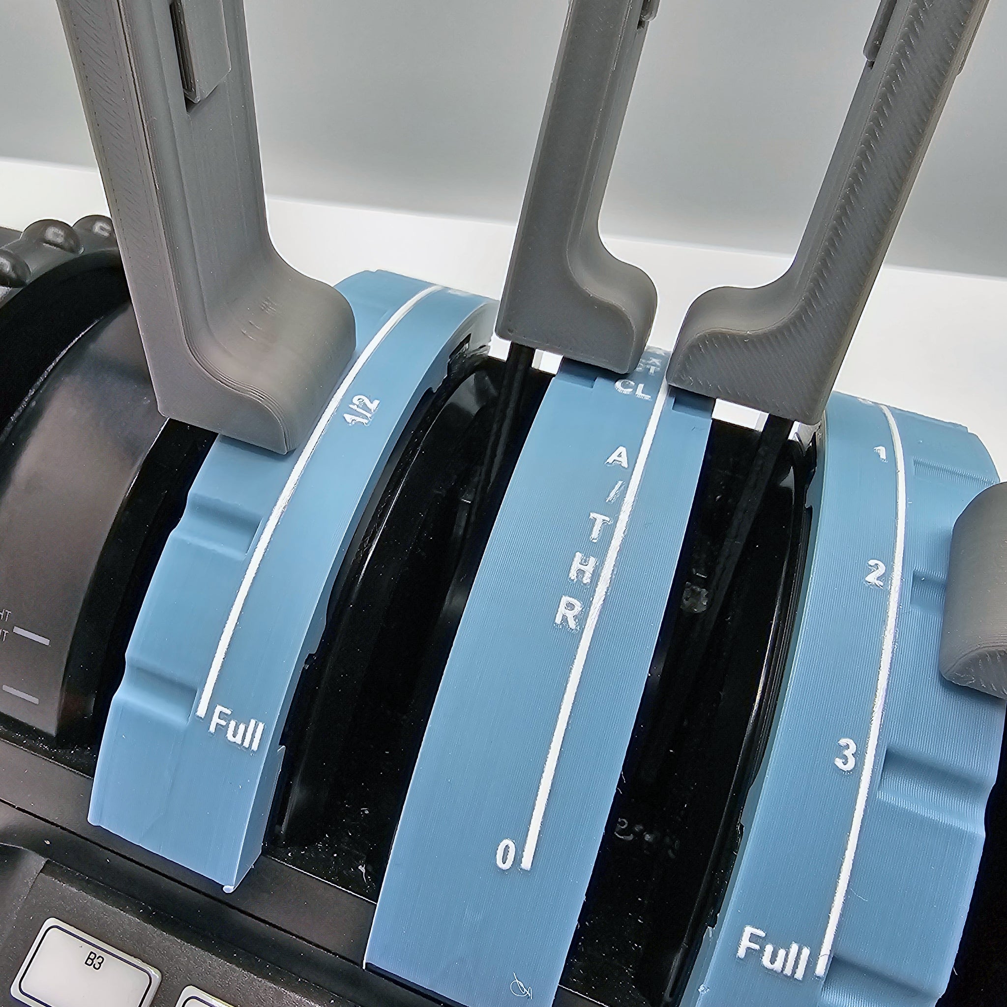 Close-up of the Airbus Functional Addon for Turtle Beach Velocity One by Prodesksim, featuring a throttle quadrant with four levers, ideal for flight simulation enthusiasts. Two blue levers are marked "1/2" and "Full," showcasing white numerals and a tactile wavy texture. The central gray handle is labeled "A/THR," evoking an authentic Airbus addon experience. Black buttons are visible at the bottom.