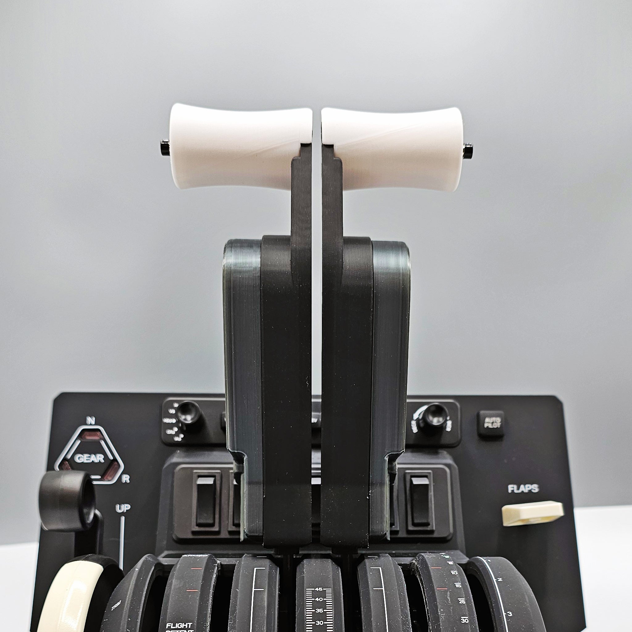 Close-up of a Honeycomb Bravo throttle quadrant, showcasing two white levers at the top along with a range of black controls below, including switches and a flaps lever. Ideal for elevating your flight simulation experience with the NEW! ProDeskSim Boeing 777 Advanced Full Package Addon for Honeycomb Bravo and Flight Simulator by Prodesksim. The background is blurred gray, reminiscent of the sleek design associated with Boeing 777 addons.