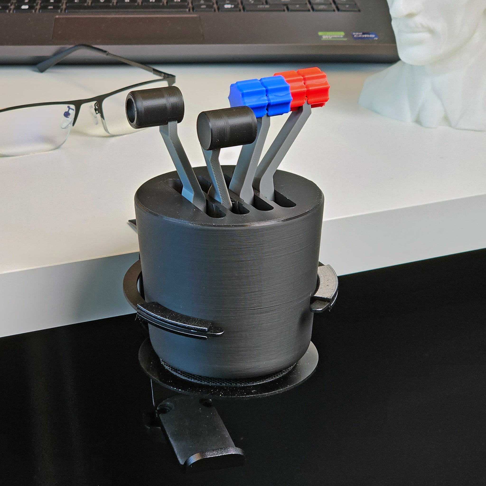 Introducing the G58 Baron - The Cup Holder Flight Fidget by FlightFidgets.com: This black pen holder, ingeniously designed to resemble a joystick control system, serves as both a stylish organizer and a fidgeting gadget for aviation enthusiasts. It boasts five levers—three in striking red and two in calming blue—and complements any workspace when placed next to your laptop, glasses, and white statuette head.