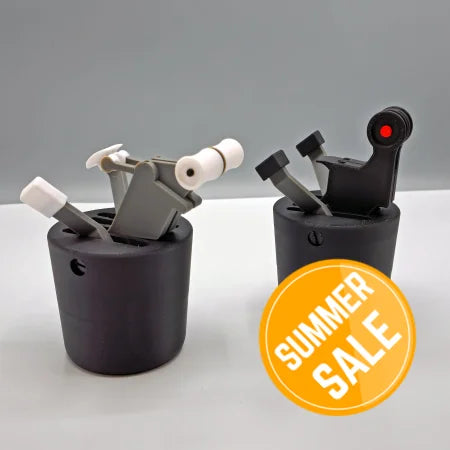 The Save More! Boeing 737 + Airbus - The Cup Holder Flight Fidget by FlightFidgets.com presents a captivating sensory experience with two black cylindrical designs featuring mechanical levers and components against a gray backdrop. The piece on the left incorporates white and gray elements, while the one on the right showcases a bold black and red color palette—ideal for airplane enthusiasts seeking distinctive design appeal.