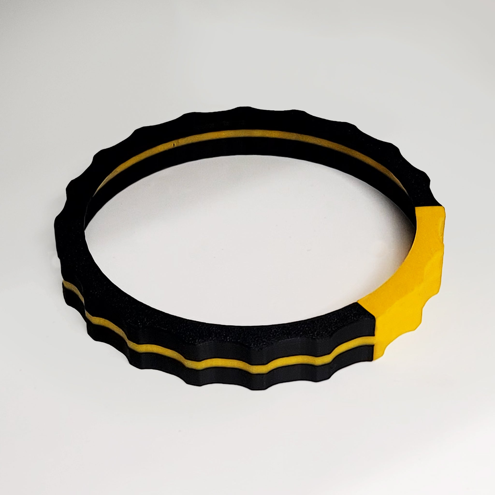 The Prodesksim Vibrant Trim wheel cover for Honeycomb Bravo Throttle Quadrant, featuring a round, ridged design in black with a yellow stripe and section, rests on a plain white surface.