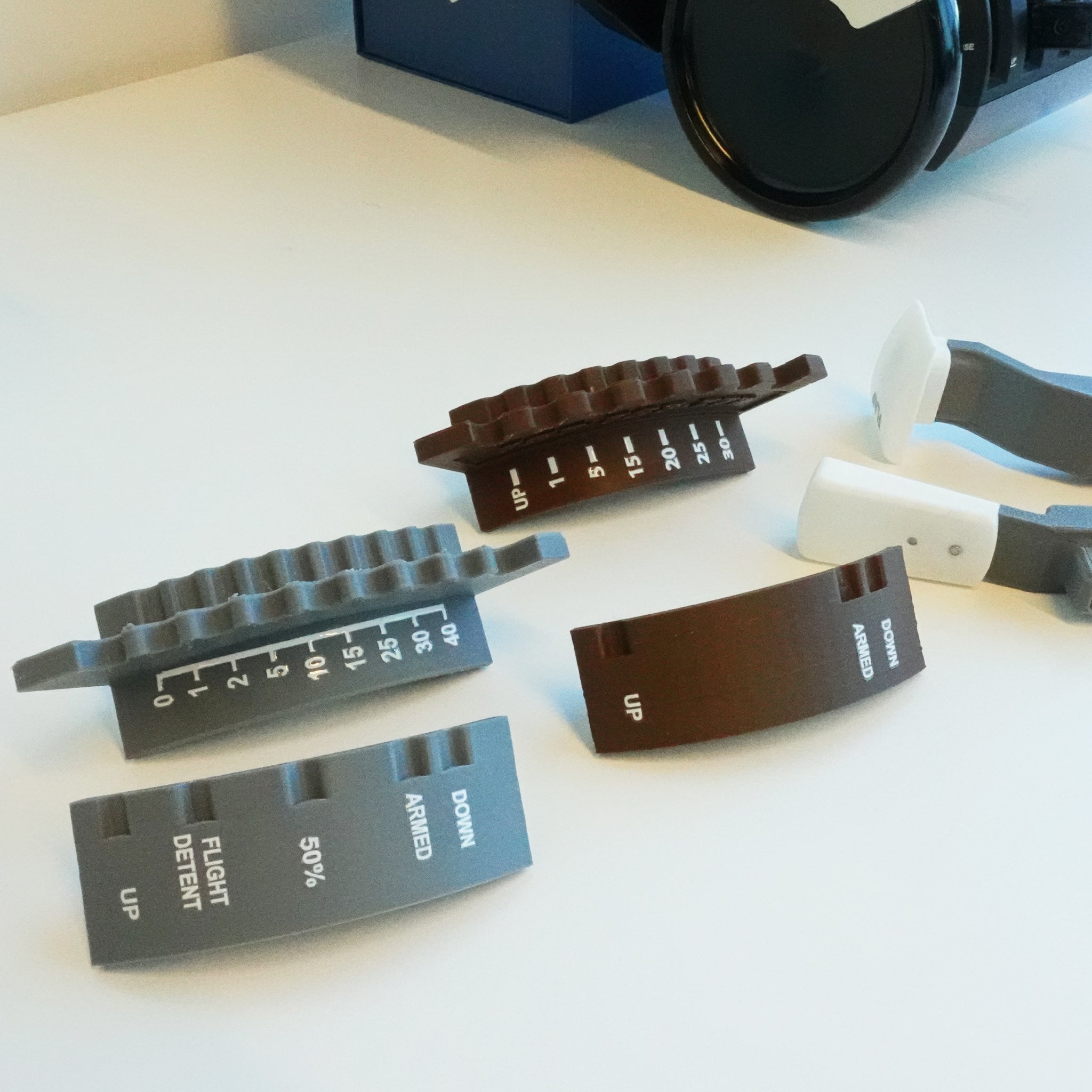 A display of 3D-printed mechanical parts in gray and brown, featuring labels such as "DOWN," "ARMED," and "FLIGHT DETENT," highlights a dual action design. These components are arranged on a white surface with Prodesksim's Boeing 777 Dual Action Detent/Spring mechanism flaps and Detent realistic speed brake Professional addon for HoneyComb Bravo throttle/VR nearby, providing an intricate glimpse into innovation.