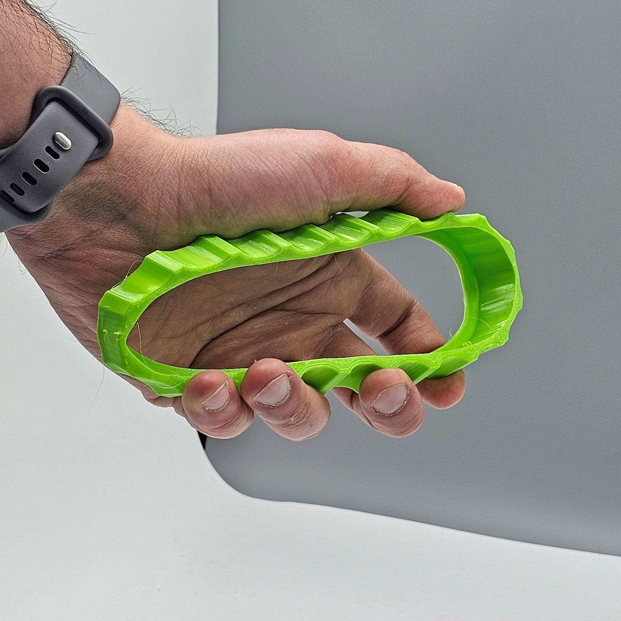 A person wearing a gray smartwatch holds a vibrant green trim wheel cover from Prodesksim, designed for the Honeycomb Bravo Throttle Quadrant and featuring a honeycomb-like pattern with ridged sides. The object is set against a gray background, with the fingers wrapping around it comfortably.