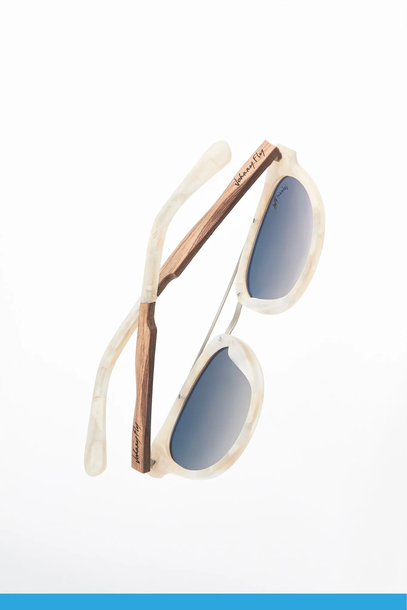 The Captain sunglasses by Johnny Fly, featuring marble-patterned acetate front sections and wooden arms, are displayed against a white background. The blue-tinted polarized lenses are round, providing a stylish and contemporary look.