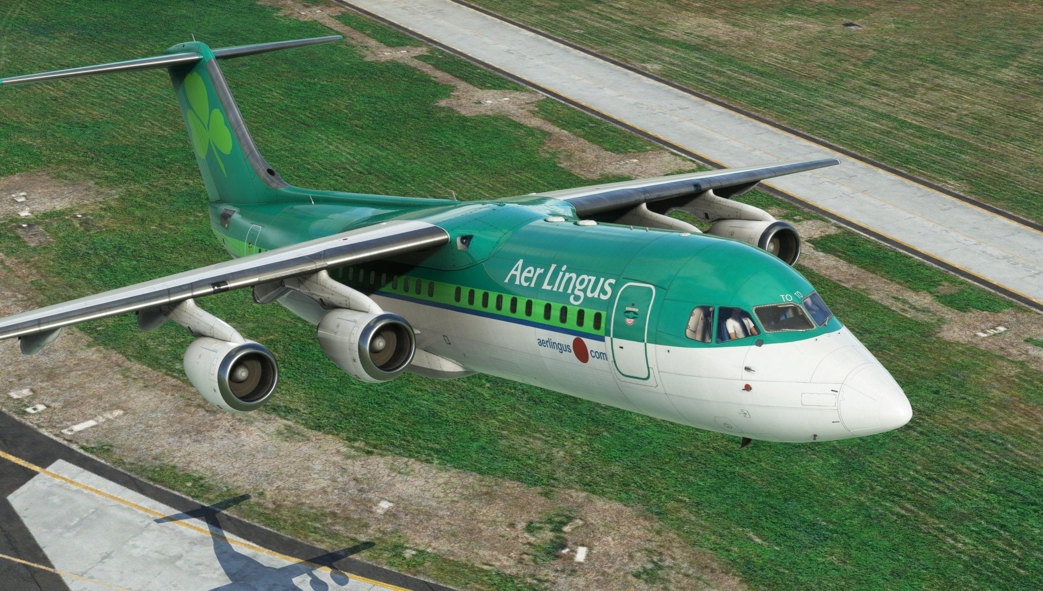 A Just Flight BAE-146 Professional aircraft from MSFS2020 gracefully flies over a grassy area near the runway. This green and white plane, featuring a shamrock emblem on its tail, offers an awe-inspiring aerial view, reminiscent of a scene captured in Microsoft Flight Simulator by Just Flight.