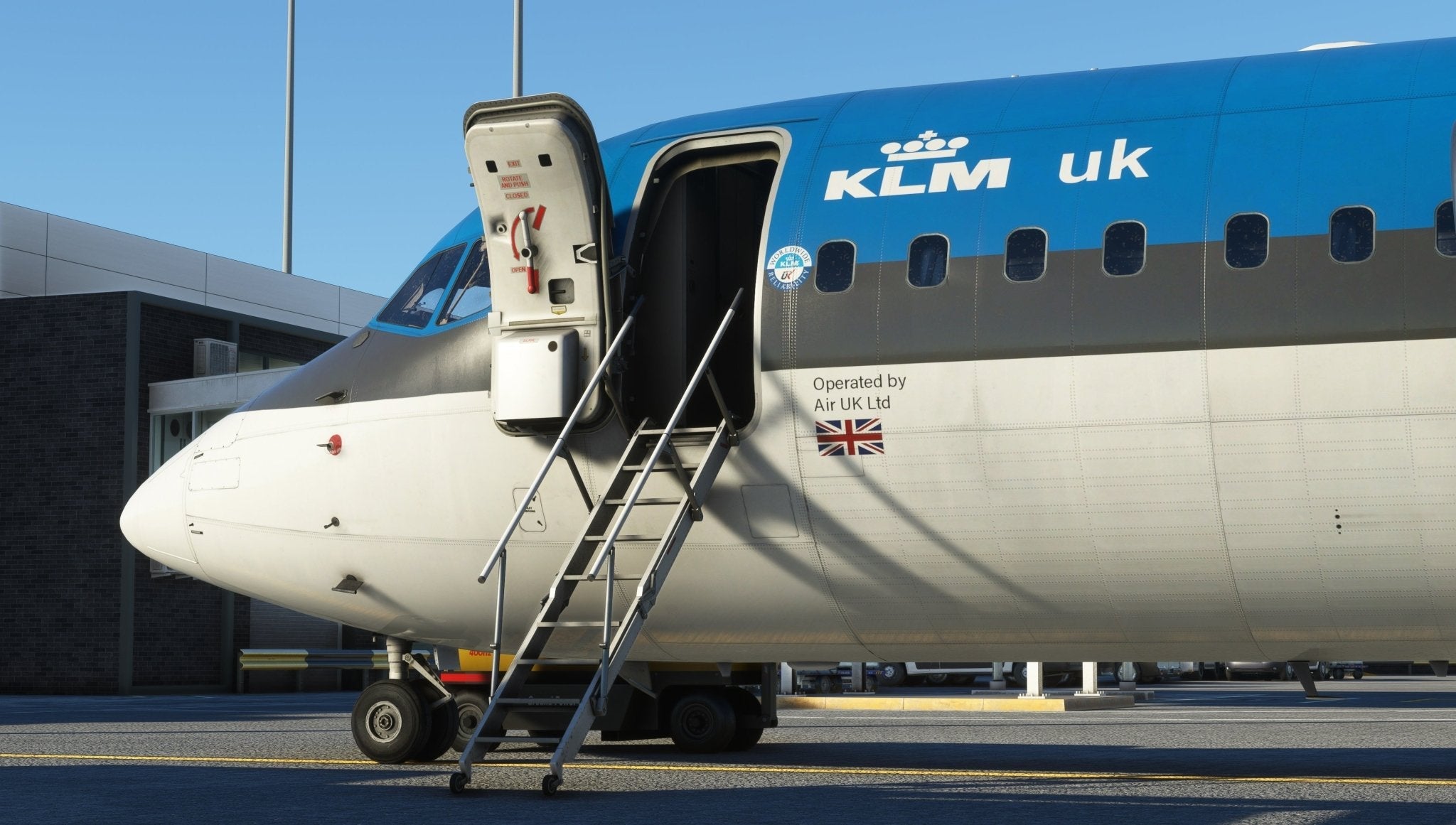 A Just Flight BAE-146 Professional for MSFS2020 aircraft, stylishly painted in black and blue, is stationed at an airport. The boarding door is open invitingly with a metal staircase connected. Near the entrance, the British flag waves proudly alongside the words "Operated by Air UK Ltd," capturing the essence of 146 Professional in MSFS by Just Flight.