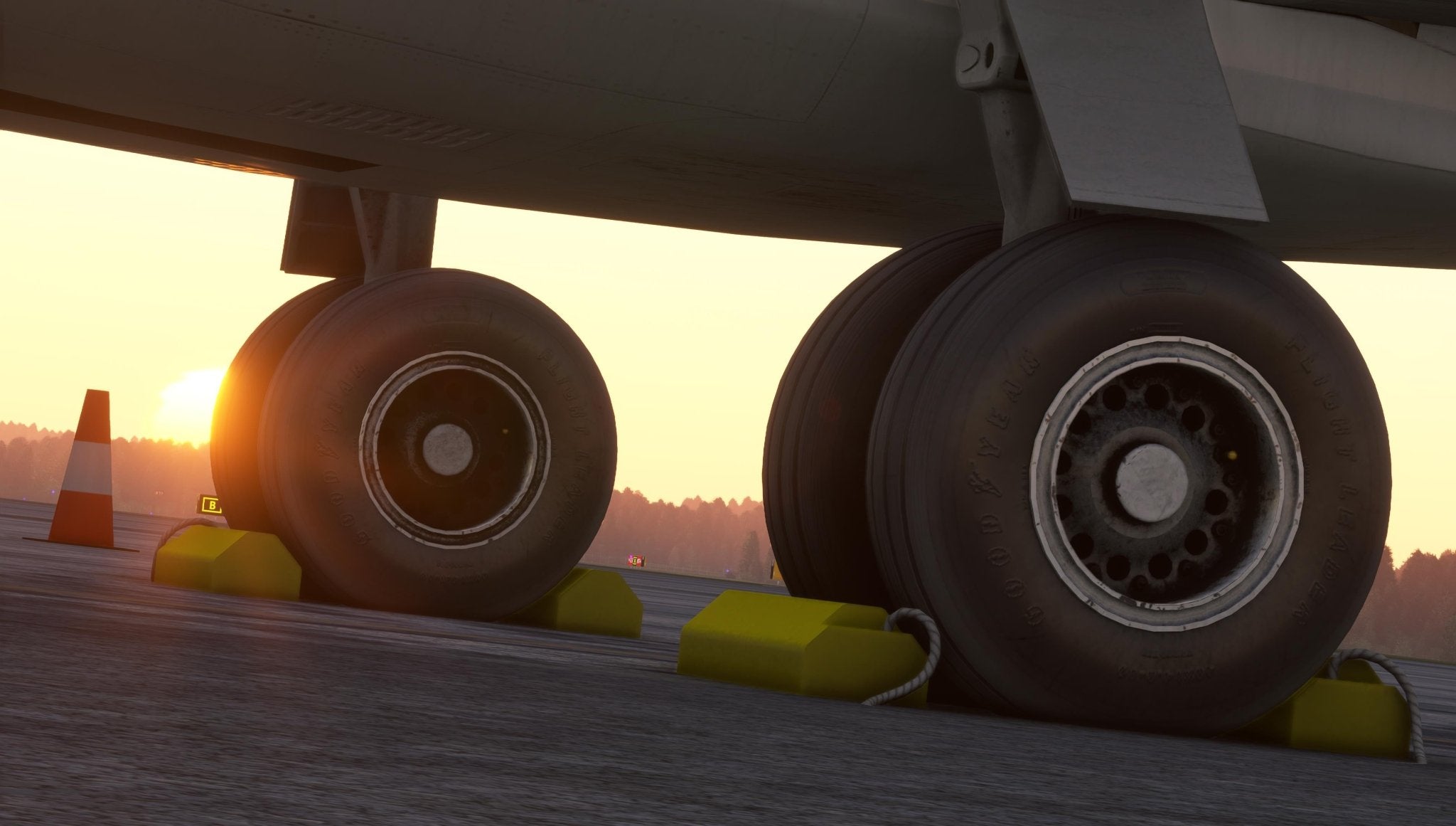 A close-up of the landing gear of a Just Flight Fokker-28 Professional for MSFS2020 regional jet resting on a tarmac at sunset. The sun casts a warm glow over the scene, while two bright yellow chocks secure the wheels. An orange cone stands nearby, enhancing this picturesque moment with Just Flight's offering.