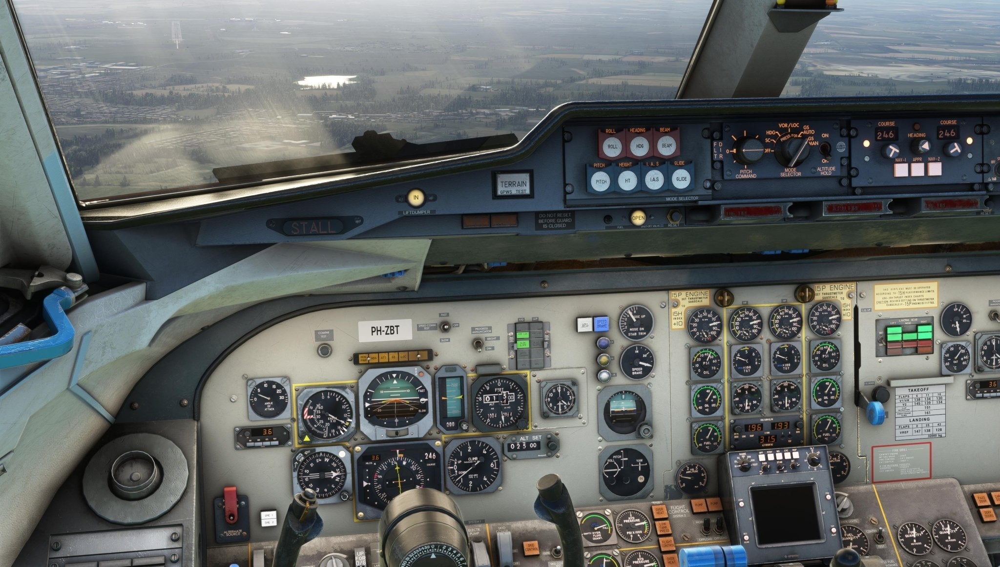 In the cockpit of a Just Flight Fokker-28 Professional for MSFS2020, numerous controls, dials, and gauges line the panels. Through the windows, a patchwork landscape of fields unfolds below, with a small body of water shimmering under the cloudy sky.