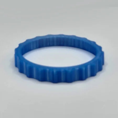 A vibrant and flexible trim wheel cover by Prodesksim, designed for use with the Honeycomb Bravo Throttle Quadrant, is captured upside down on a smooth, light gray surface, showcasing its precision and blue plastic ribbed edge.