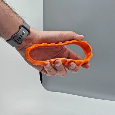 A person wearing a gray watch holds an orange, oval-shaped object with a textured grip similar to the 1 Color Vibrant and Flexible Trim Wheel Cover for the Honeycomb Bravo Throttle Quadrant by Prodesksim. The background is a plain gray surface, subtly contrasting its sleek design and enhancing its appeal for flight simulation enthusiasts.
