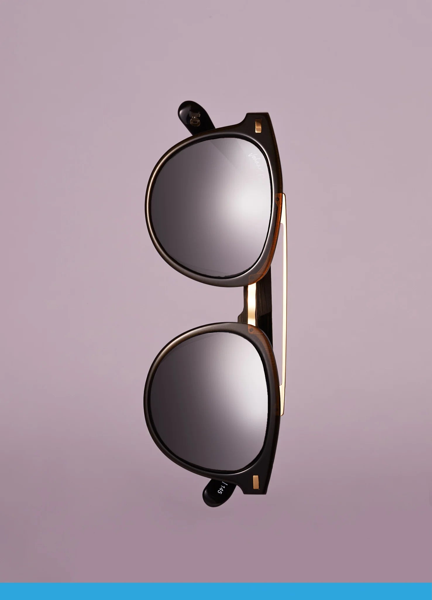 The Johnny Fly Captain sunglasses, featuring a sleek acetate front and mirrored polarized lenses, are positioned vertically against a solid light purple background. This creates an elegant and sophisticated look.