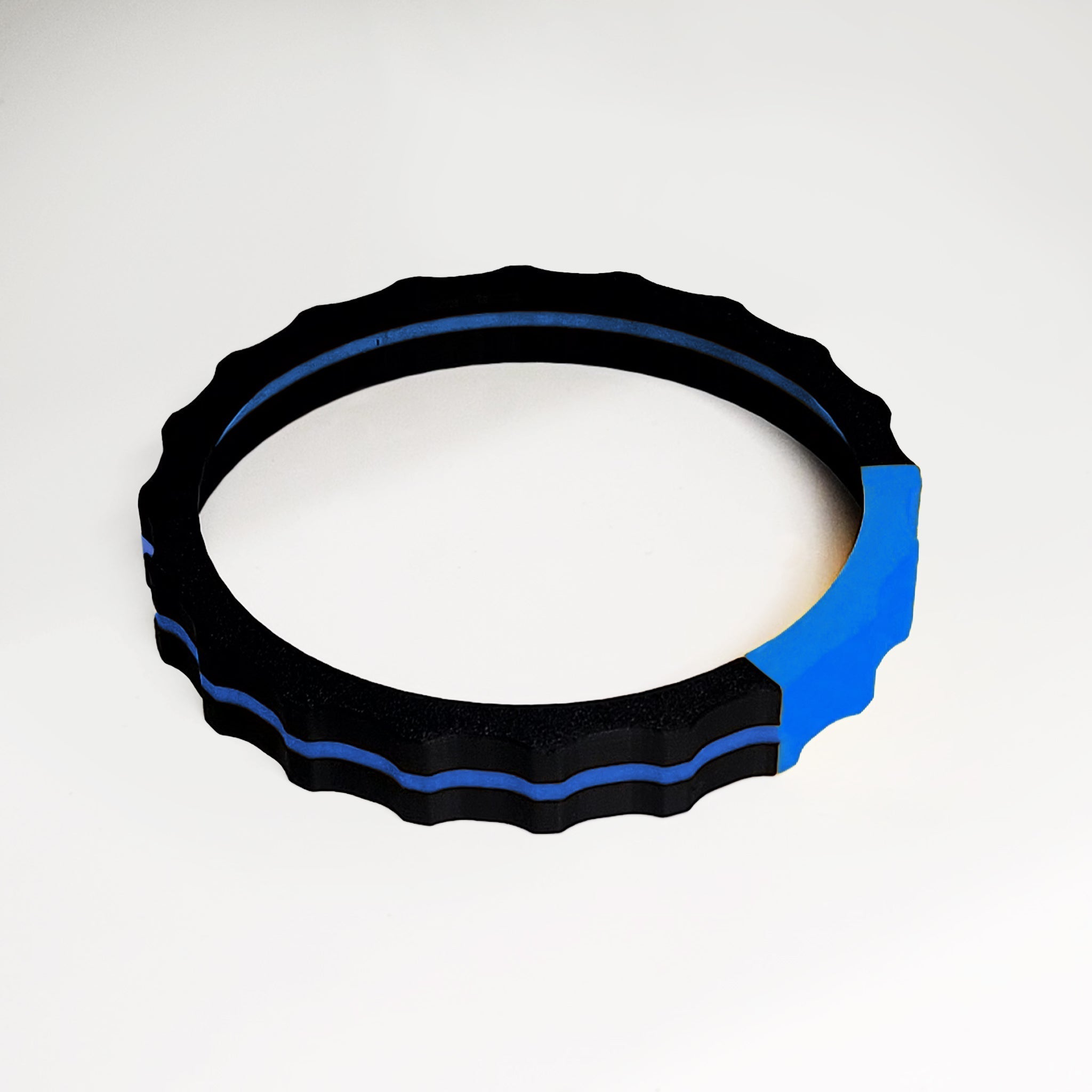 A Prodesksim 2 Color TRIMER, featuring a circular ring with a wavy outer edge in black and blue, sits on a light surface. The minimalist design of this vibrant trim wheel cover for the Honeycomb Bravo Throttle Quadrant highlights the subtle blue segment against the predominant black, capturing the sleek essence of flight simulation gear.