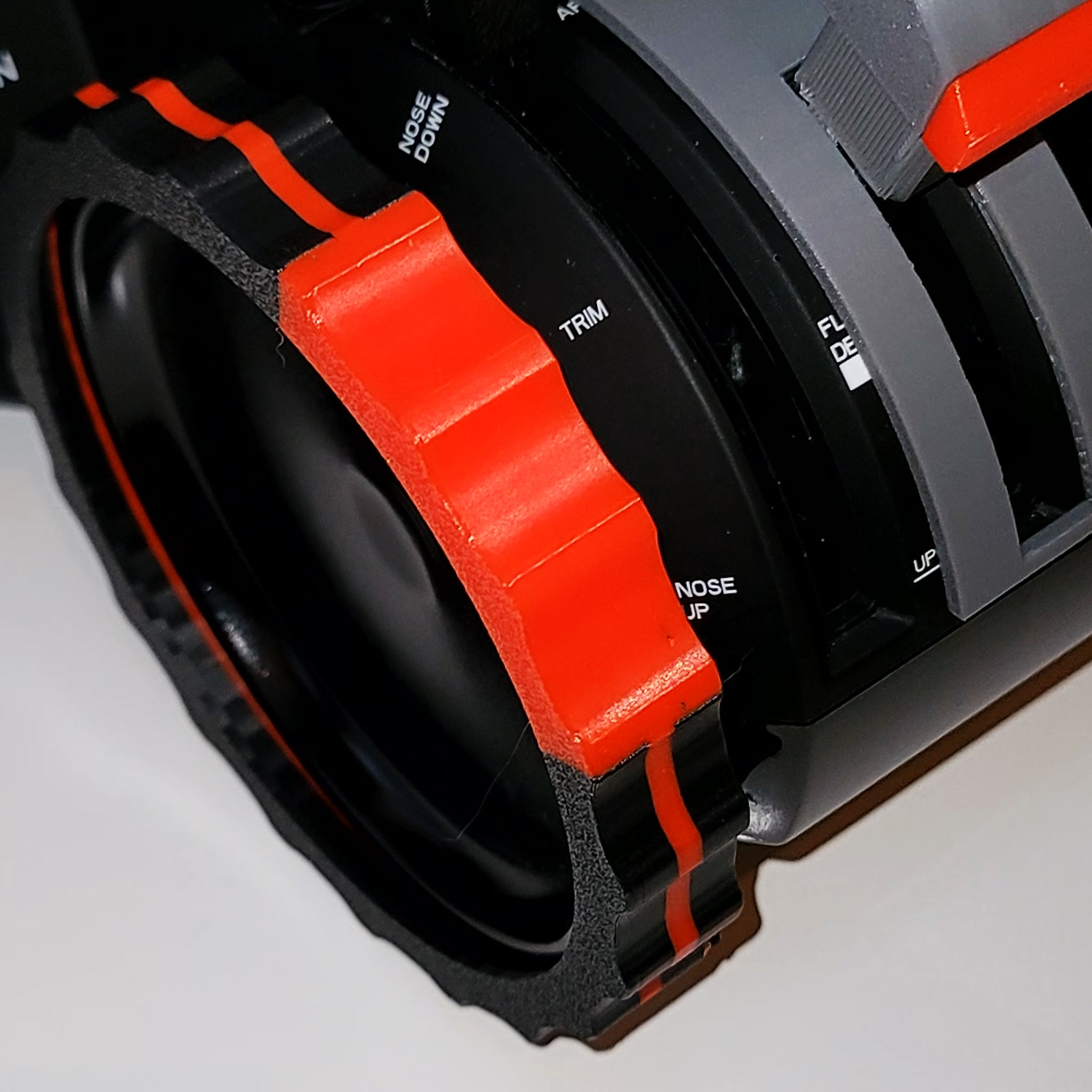 The distinctive black and red dial, adorned with a ridged edge and labeled "TRIM," "NOSE DOWN," and "NOSE UP," is part of the Prodesksim 2 Color TRIMER - Vibrant Trim wheel cover for the Honeycomb Bravo Throttle Quadrant. Its gray mechanism includes additional markings that enhance the realism of your flight simulation experience.