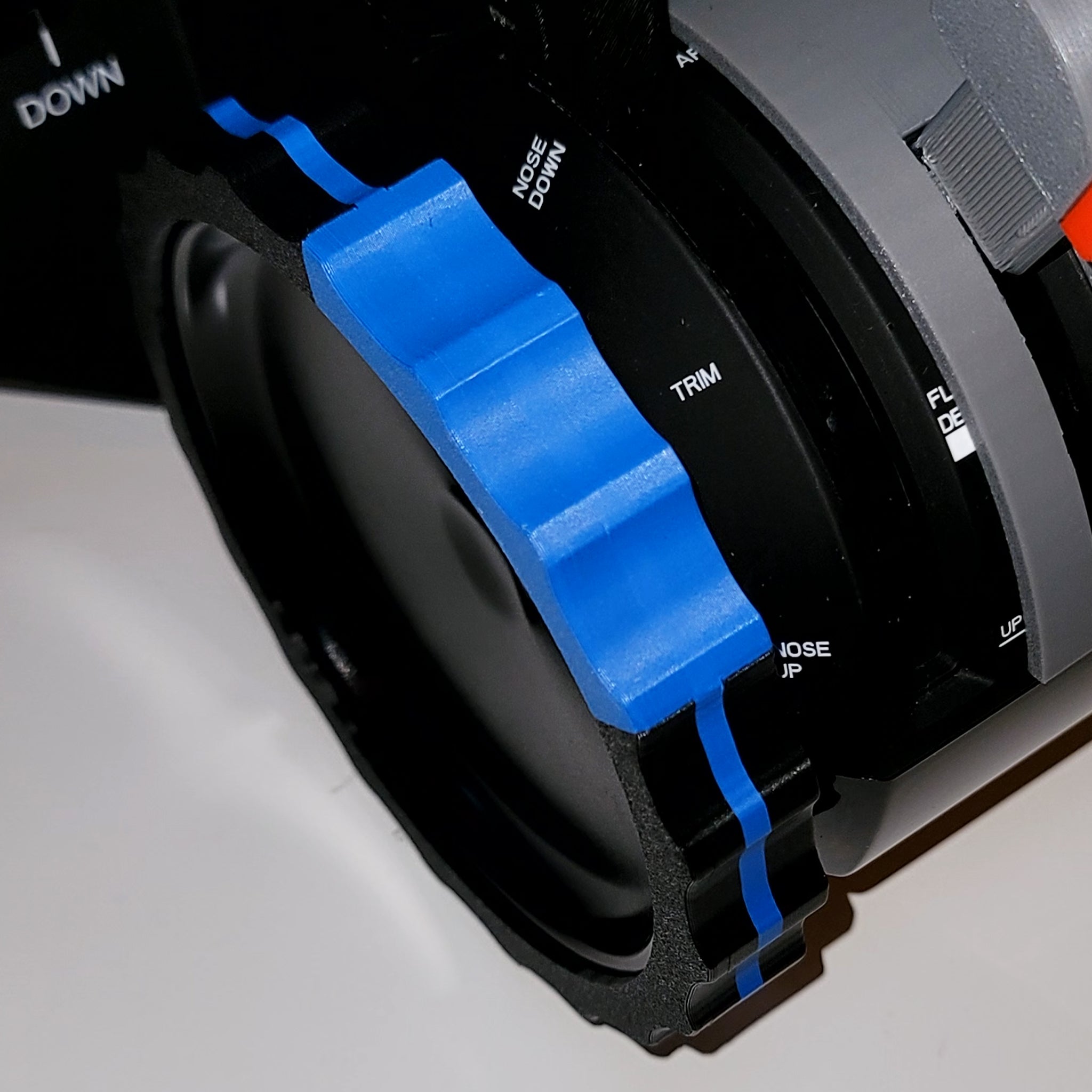 A close-up of a camera lens with a textured ring, similar to the precision found in flight simulation setups. The black ring features a bright blue grip and labels like "TRIM" and "NOSE UP," reflecting the industrial design seen in Prodesksim's NEW! ProDeskSim Full Boeing Advanced Full Package addons for Honeycomb Bravo throttle levers.