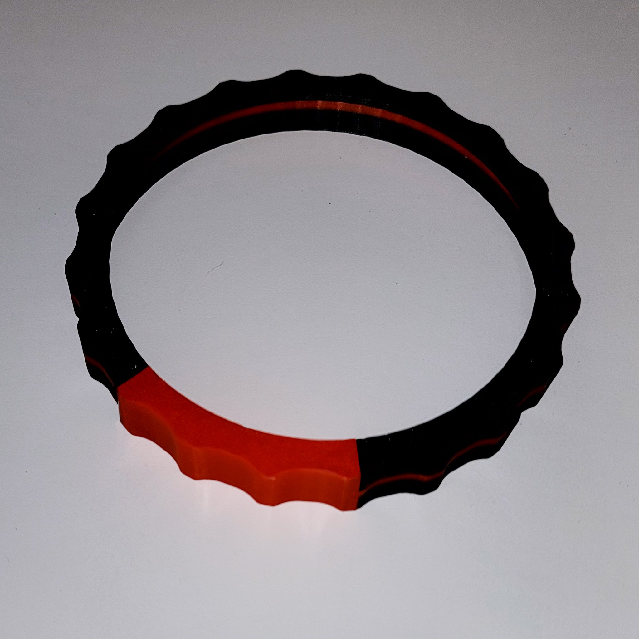 A flat, circular object featuring a wavy-edged design, this Prodesksim 2 Color TRIMER is primarily black with a striking red segment. It rests on a plain white surface and casts a faint shadow—an ideal accessory for Honeycomb Bravo throttle quadrant users and flight simulation enthusiasts.