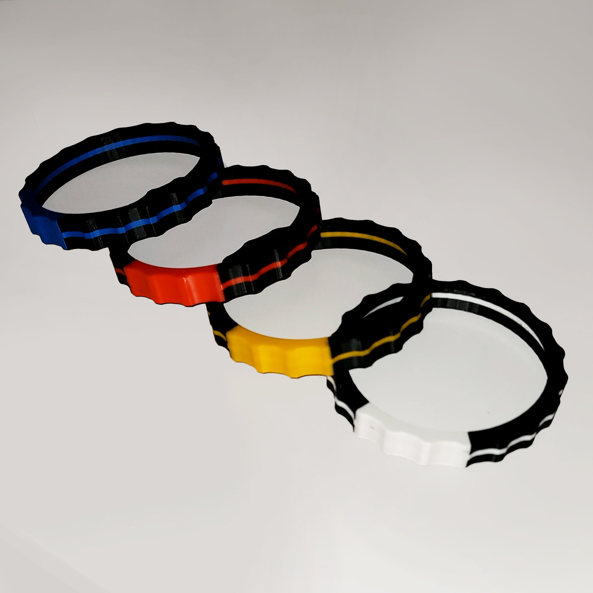 A set of four interlocking rings in blue, red, yellow, and white are arranged diagonally on a light background. Each ring's wavy, segmented design reflects the tactile precision of a Prodesksim 2 Color TRIMER - Vibrant Trim wheel cover for Honeycomb Bravo Throttle Quadrant used in flight simulations, adding texture and depth to this dynamic composition.