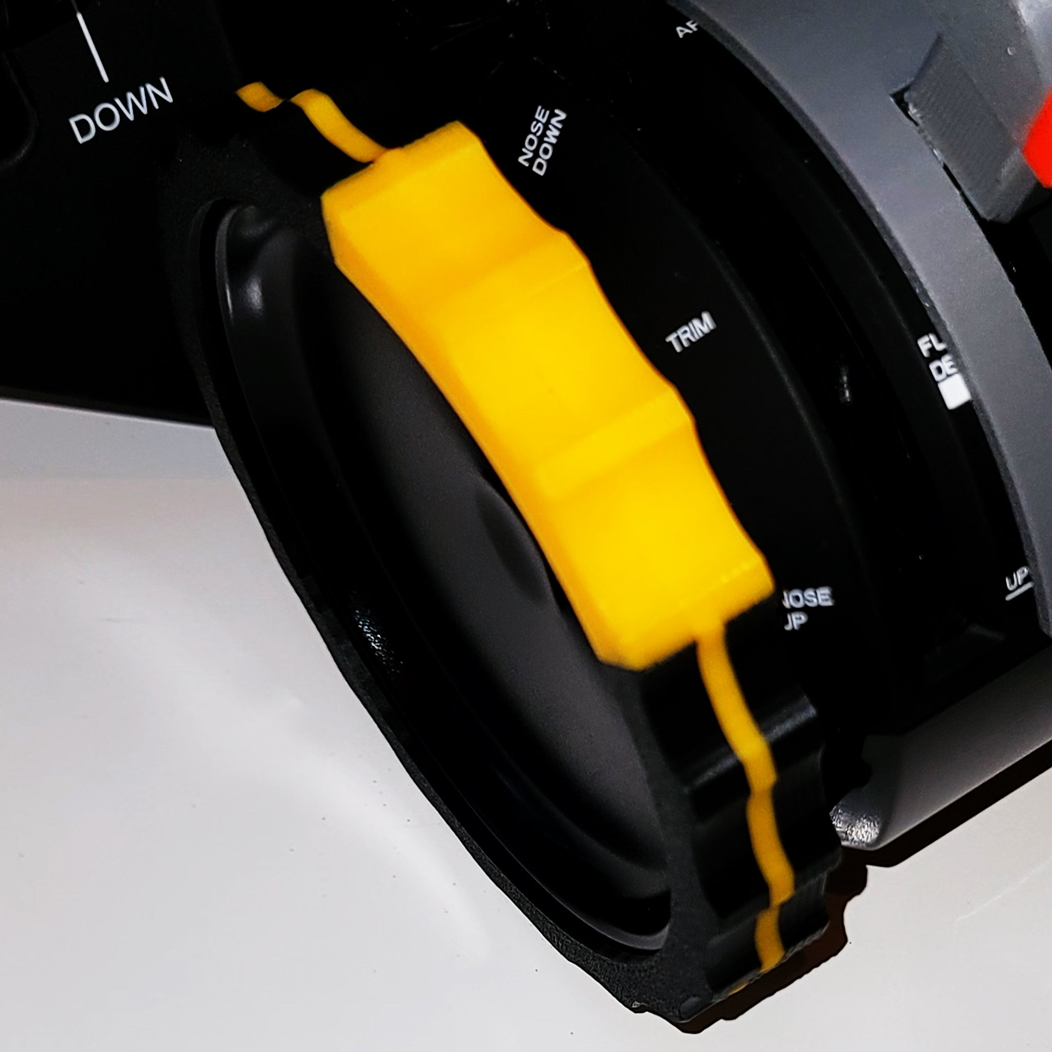 Close-up of a black and yellow control knob on a Honeycomb Bravo Throttle Quadrant, featuring labels such as "DOWN," "TRIM," and "NOSE DOWN," with the premium 2 Color TRIMER by Prodesksim. The knob, equipped with a textured grip ideal for flight simulation, is mounted on a smooth surface.