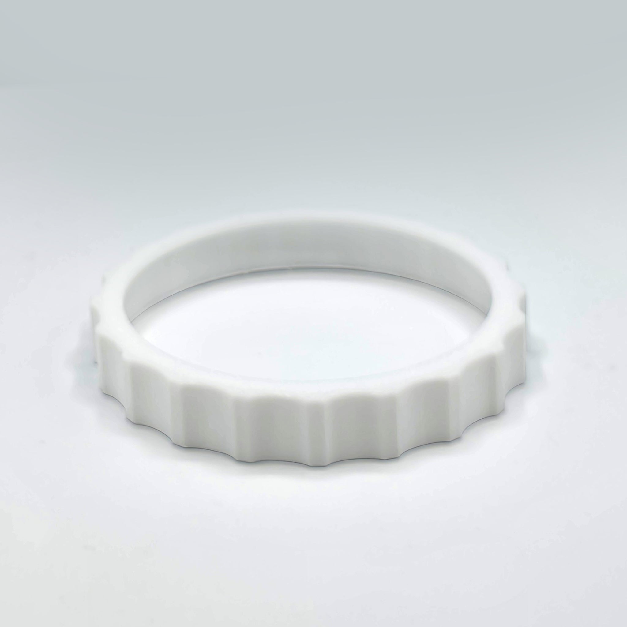 A white, circular object with a ridged edge, akin to the 1 Color Vibrant and Flexible Trim Wheel Cover for the Honeycomb Bravo Throttle Quadrant by Prodesksim, lies flat on a plain gray surface.
