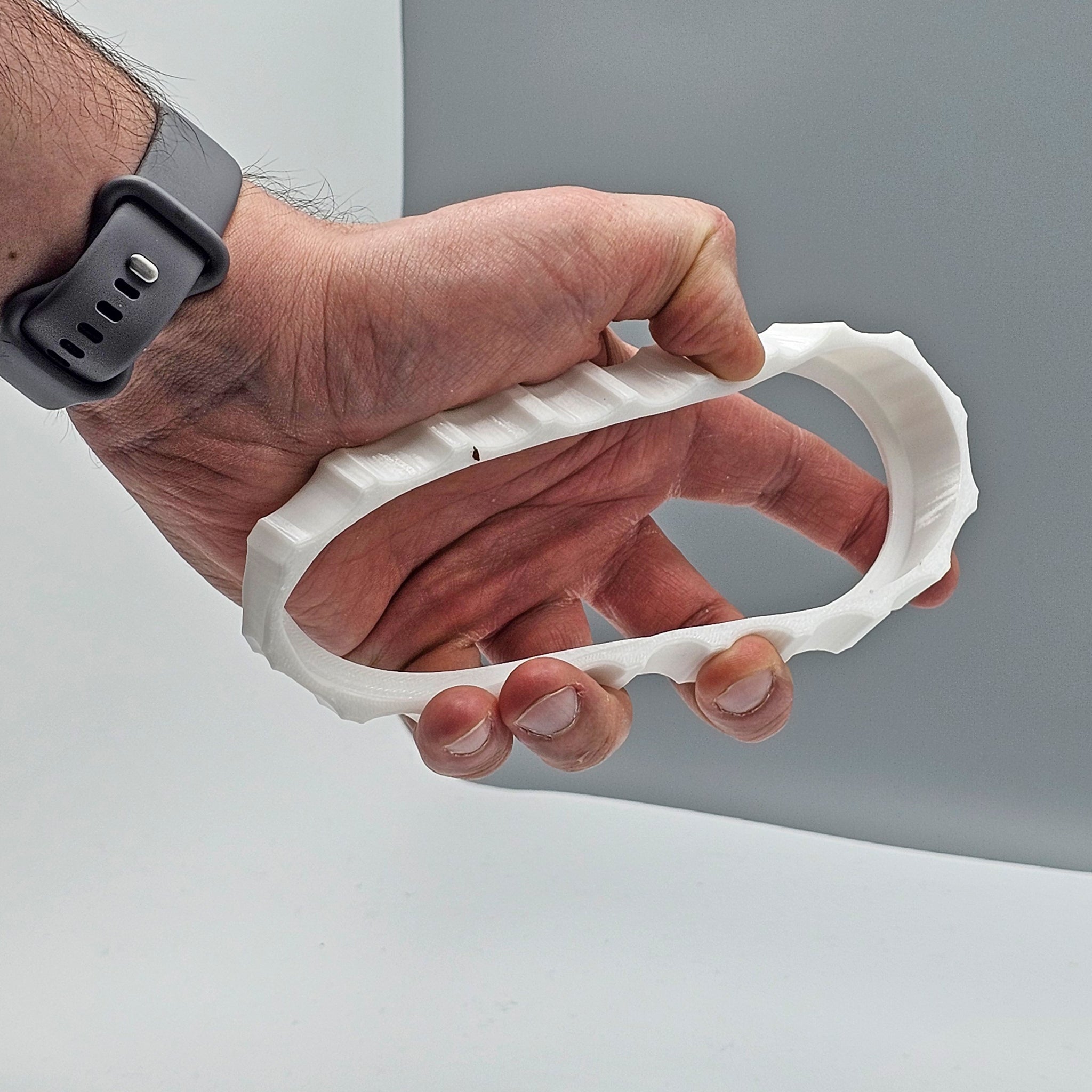 A hand is holding a white, oval-shaped, textured object against a gray background. The object looks like the 1 Color Vibrant and Flexible Trim Wheel Cover from Prodesksim. The person is wearing a gray wristwatch, suggesting their interest in flight simulation or the Honeycomb Bravo Throttle Quadrant.