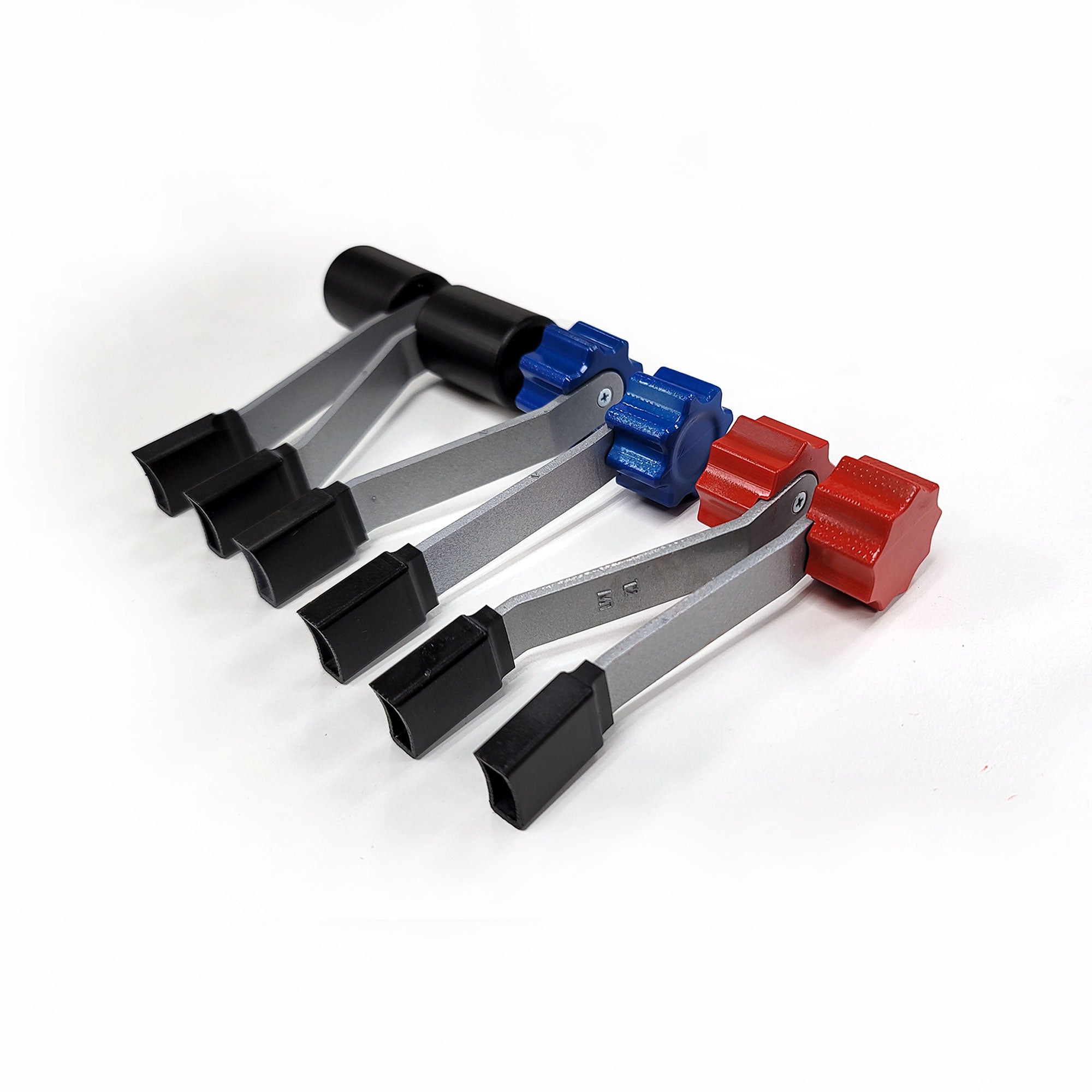 Three plastic spring clamps placed side by side on a white background emulate the precision of a Prodesksim Saitek full set throttle quadrant. Each clamp is equipped with black tips and handles, along with uniquely colored adjustment knobs—black, blue, and red—reminiscent of the controls for a twin-engine piston aircraft.